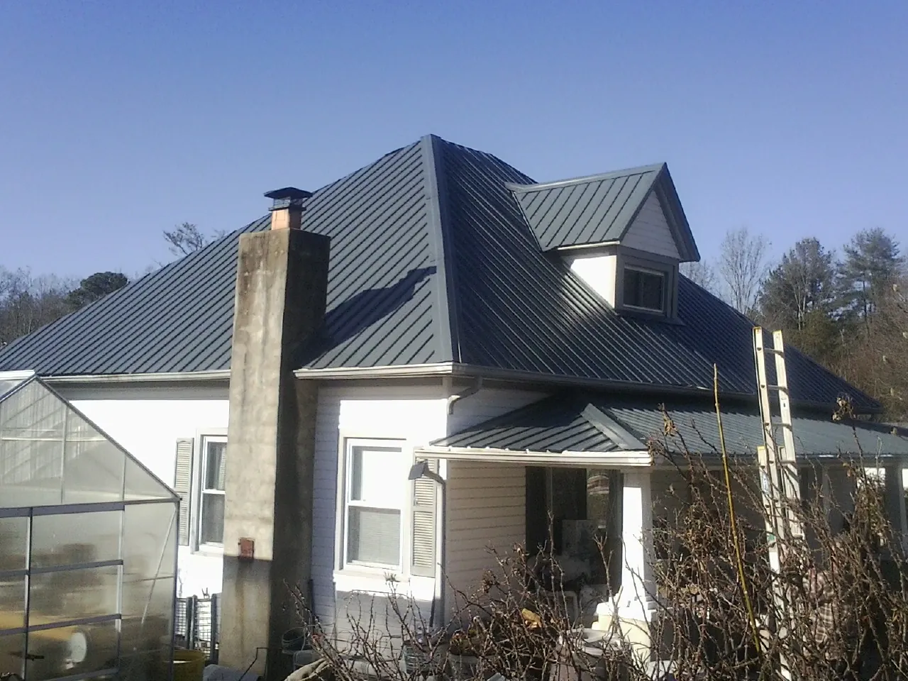 Dark blue standing seam metal roof on a white farmhouse with dormer — Slate & Tile Roof Repair by Roofing Brothers in Warners