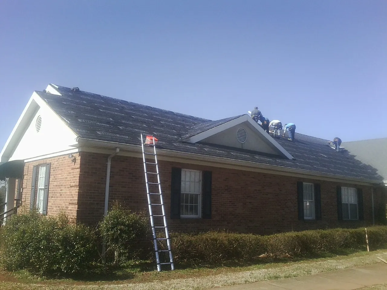 Crew tearing shingles off a brick ranch roof with a ladder set — Emergency Roof Repair work by our crew in Warners