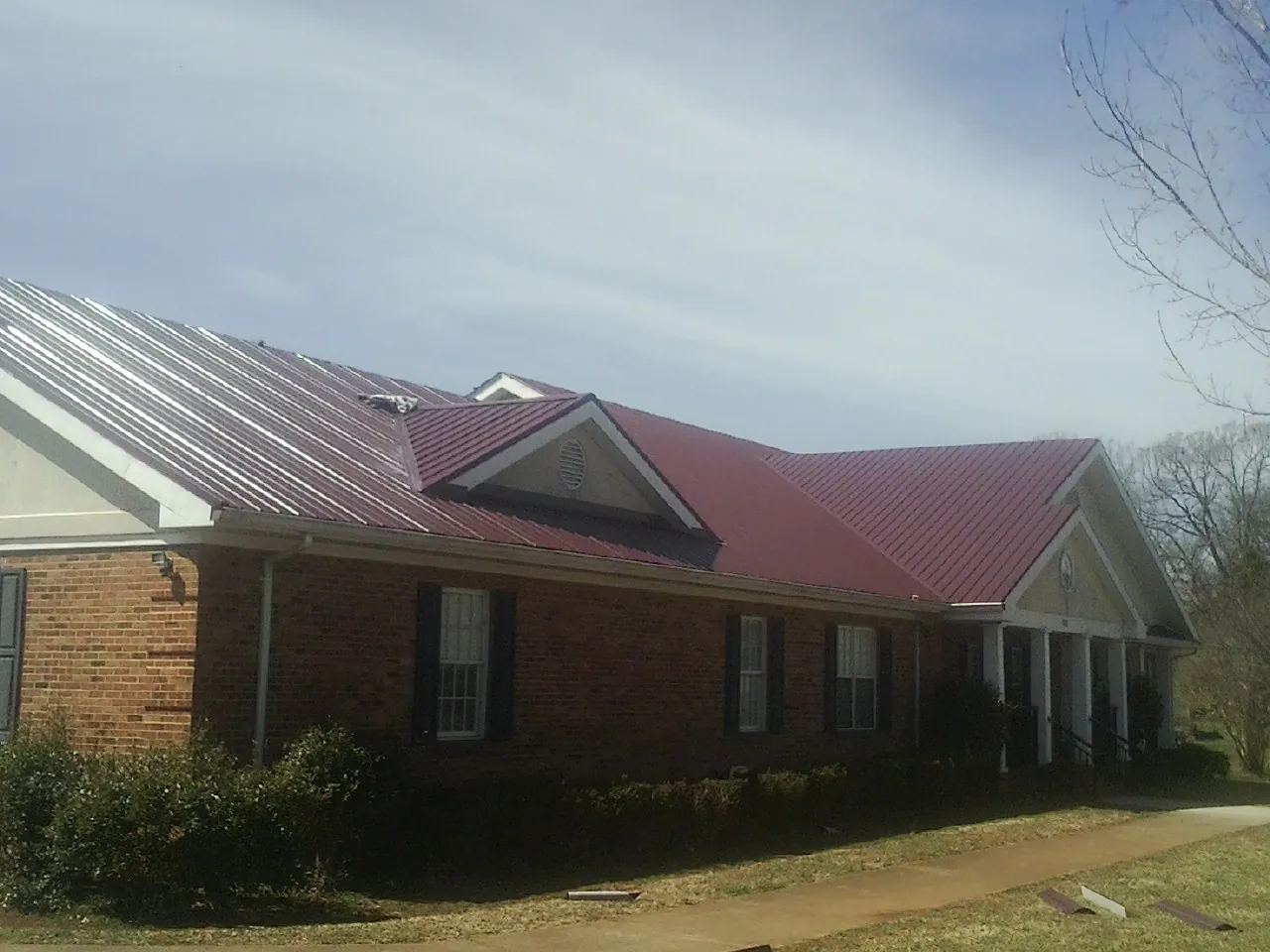 Red metal roof with gabled entries on a long brick building, from a Hail Damage Roof Repair job in Warners