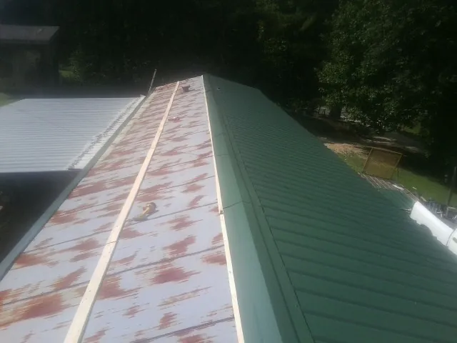 Old rusted panels beside newly installed green metal roofing — Wind Damage Roof Repair by Roofing Brothers in Warners