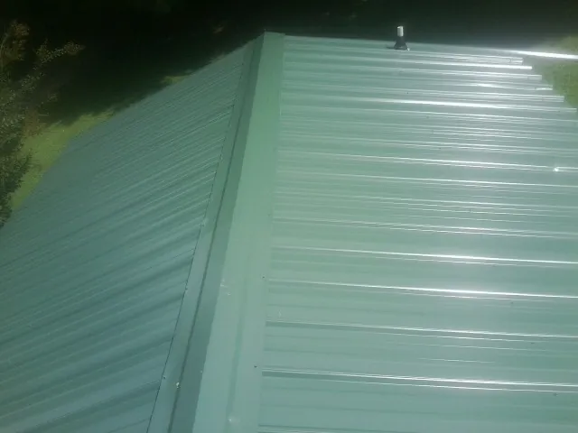 New green metal panels meeting at the ridge of a roof — Flat Roof Repair work by our crew in Warners