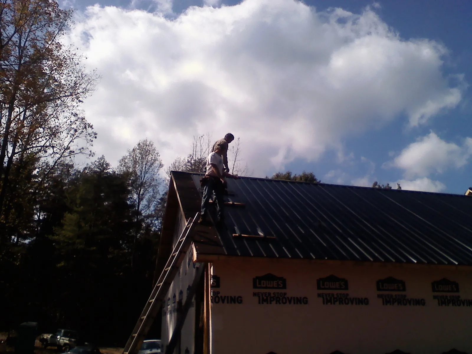 Roofer fastening dark metal panels high against a cloudy sky, from a Roof Inspection job in Warners