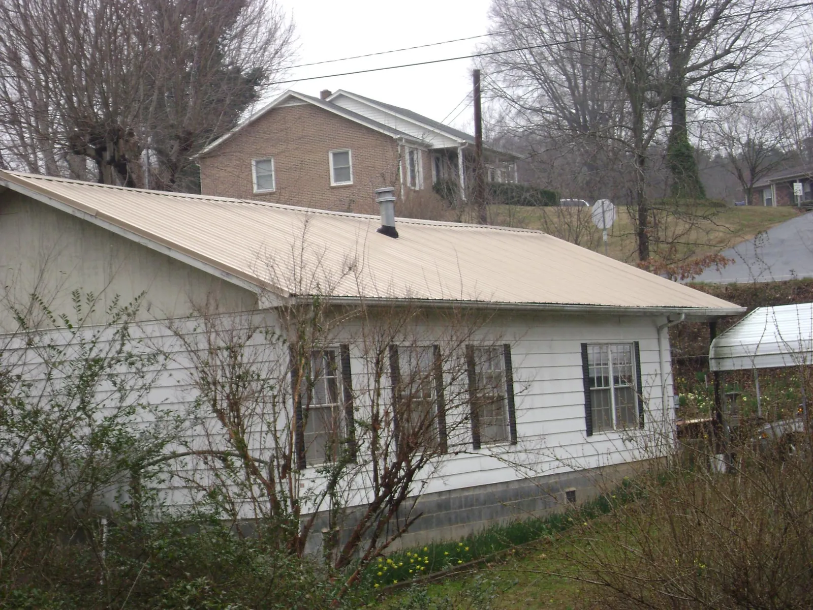 Tan metal roof on a white sided house set into a hillside — Commercial Roofing by Roofing Brothers in Warners