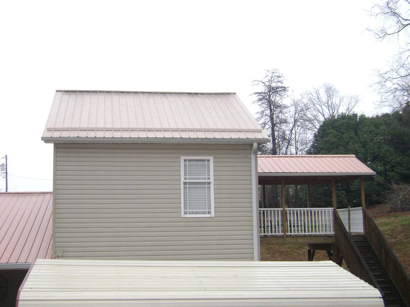 Tan metal roofs on a two story addition and attached porch, from a Roof Replacement job in Warners
